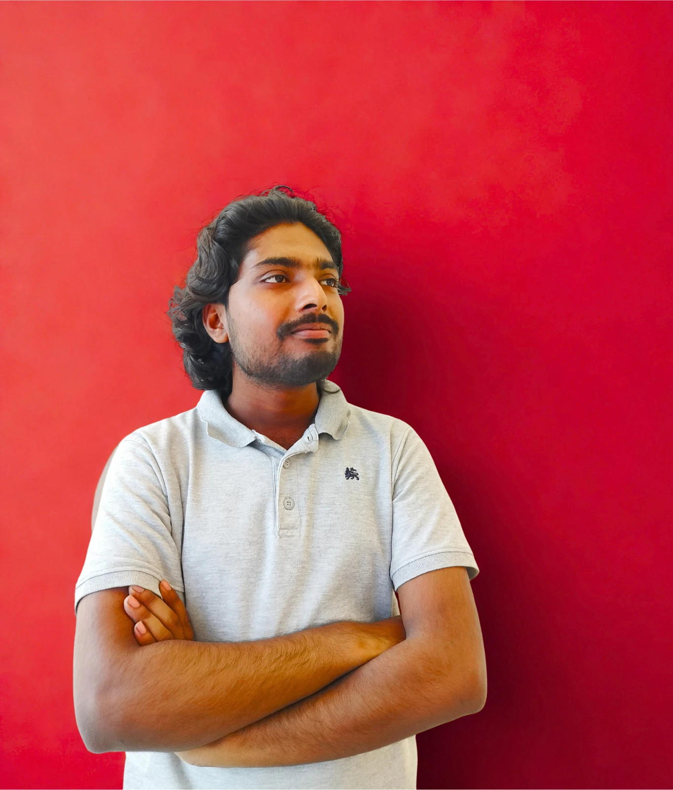 Abdullah Al Tashdid standing with folded arms against a red background
